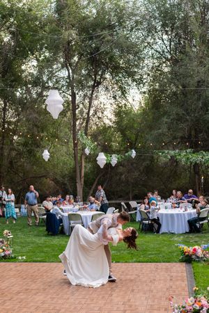 Wedding guests enjoy an outdoor reception with string lights and white lanterns in a wooded garden setting.