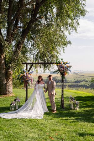 Romantic wedding ceremony moment captured under a willow tree in a scenic countryside setting with rolling hills.