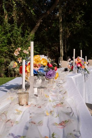 White wedding reception table settings with floral centerpieces and natural woodland backdrop create an elegant outdoor ambiance.