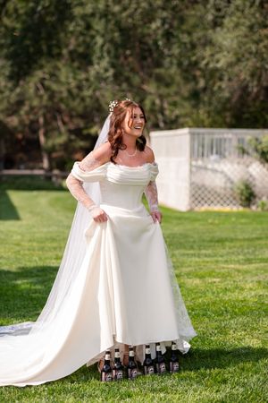 A bride in a flowing white wedding dress twirls gracefully on green grass, showing off the elegant movement of her gown.