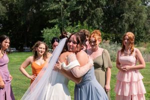 Wedding party in pink and blue dresses poses together outdoors in a garden setting during summer celebration.