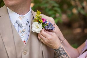 A wedding party member wears a tan suit with a colorful boutonniere made of yellow and purple flowers.