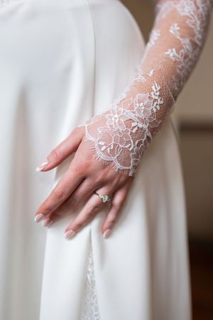 Close-up view of delicate white lace sleeves on a wedding dress with elegant hand placement against white fabric.