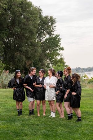 A group wearing matching black jackets stands in a line on grass with one person in white, creating a fun photo pose.