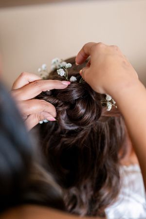 Small white flowers being pinned into dark brown hair during a wedding preparation styling session.