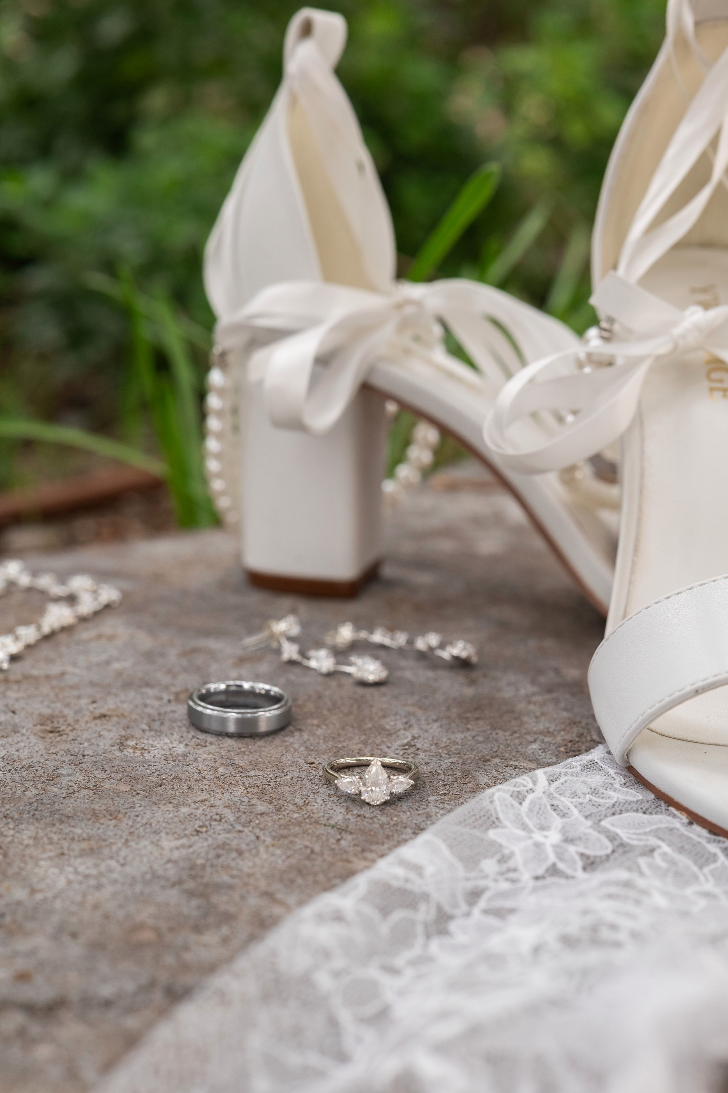 White bridal shoes and wedding rings arranged artistically on textured gray surface with delicate lace details.