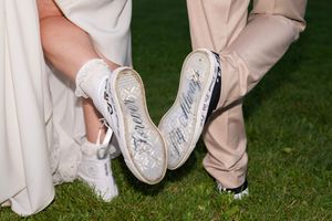 Wedding party members show off their white sneakers while standing on grass in a playful group photo.