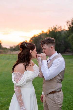 A romantic sunset wedding photo of a couple sharing a tender moment in a grassy field with trees in the background.