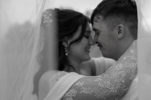 A romantic black and white wedding photo shows a tender moment between newlyweds in lace and formal attire.