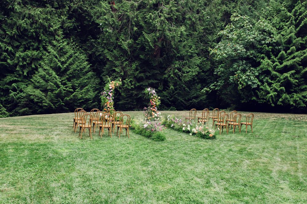 Wooden chairs arranged in rows on a lush green lawn for an outdoor wedding ceremony with floral decorations.