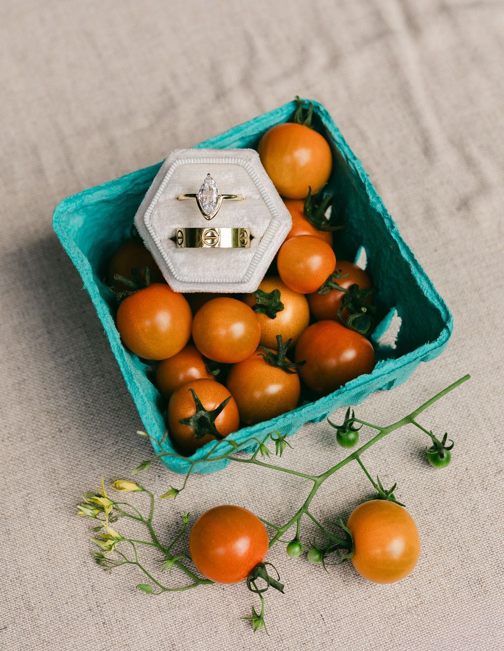 Fresh orange cherry tomatoes arranged in a turquoise paper carton with some scattered on a light gray surface.