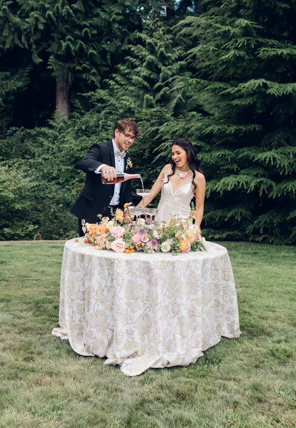 A couple shares a moment at their outdoor wedding reception table decorated with floral arrangements and white lace tablecloth.