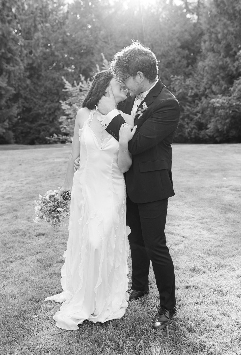Black and white wedding photo of a couple sharing an intimate moment in a garden setting.