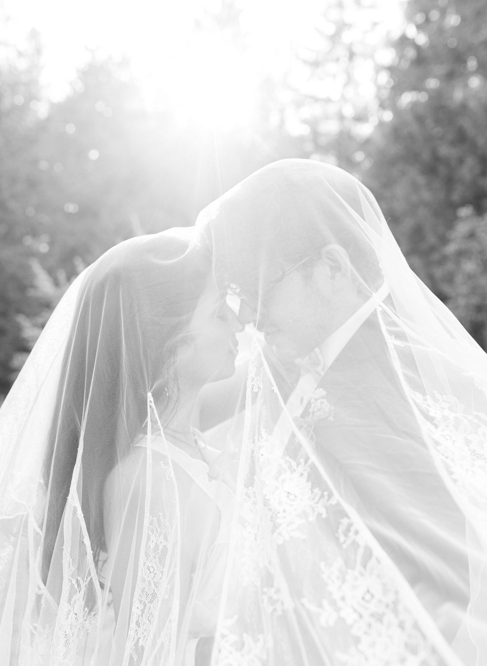 A dreamy, ethereal wedding scene with flowing white veils and soft sunlight filtering through trees.
