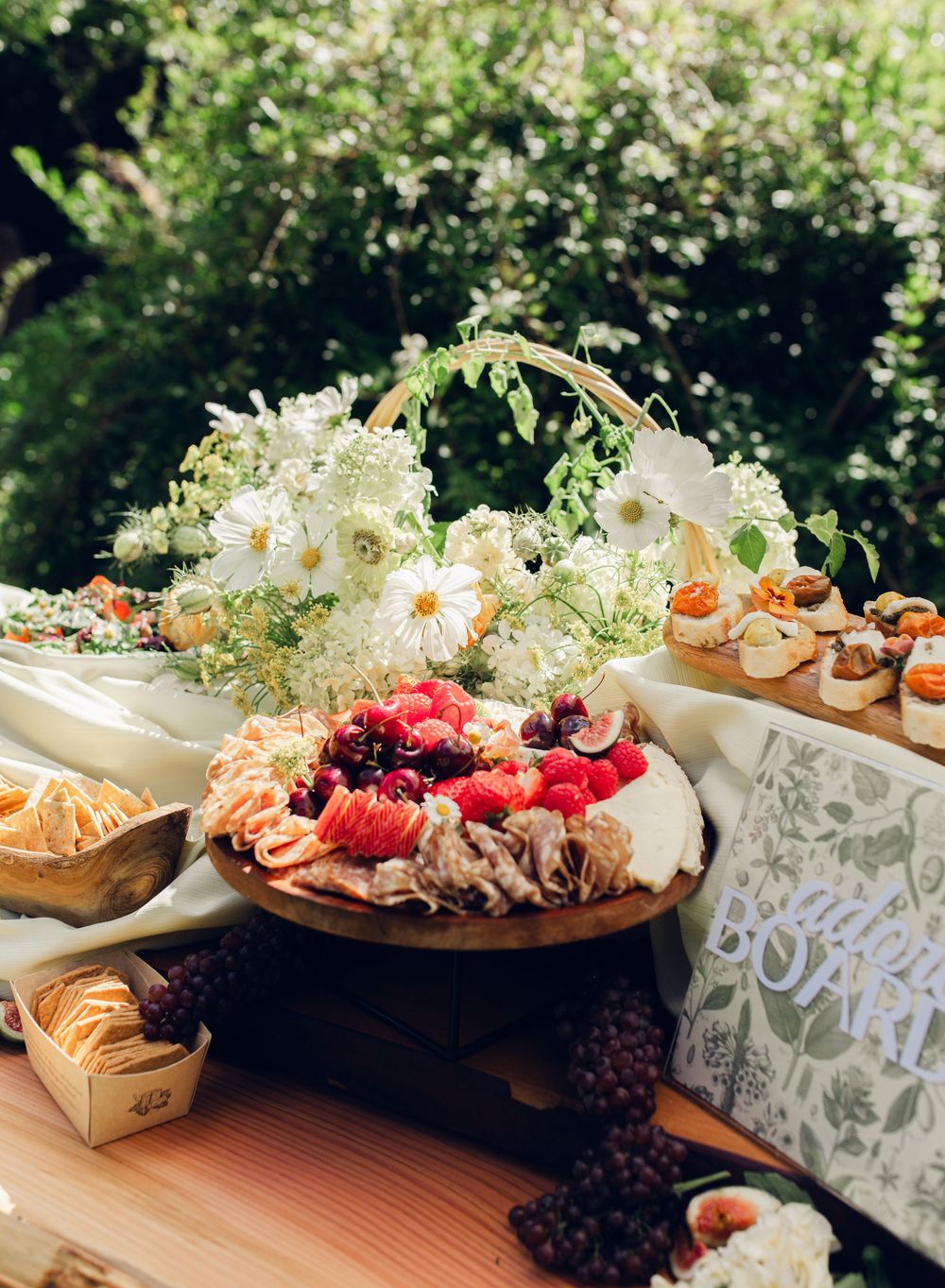 Elegant wedding reception food display with floral decorations and appetizers arranged on wooden tables.