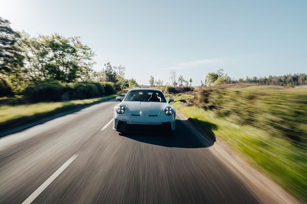 A white sports car speeds along a winding mountain road with motion blur and scenic landscape views in the background.
