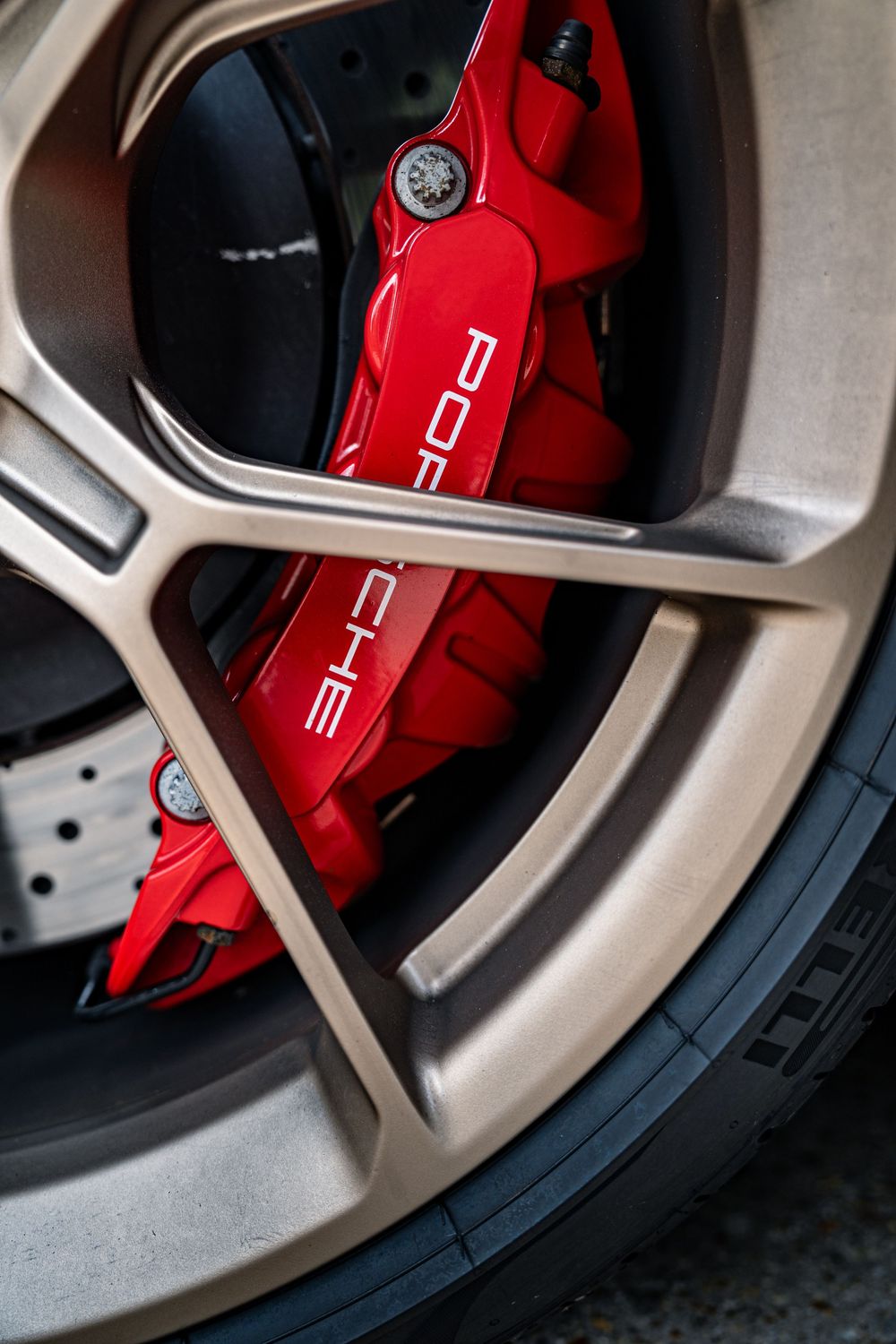 Red Porsche brake caliper visible through a silver alloy wheel spokes showing performance braking system.