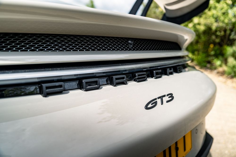 Close-up detail shot of a Porsche GT3 badge and rear grille in silver finish.