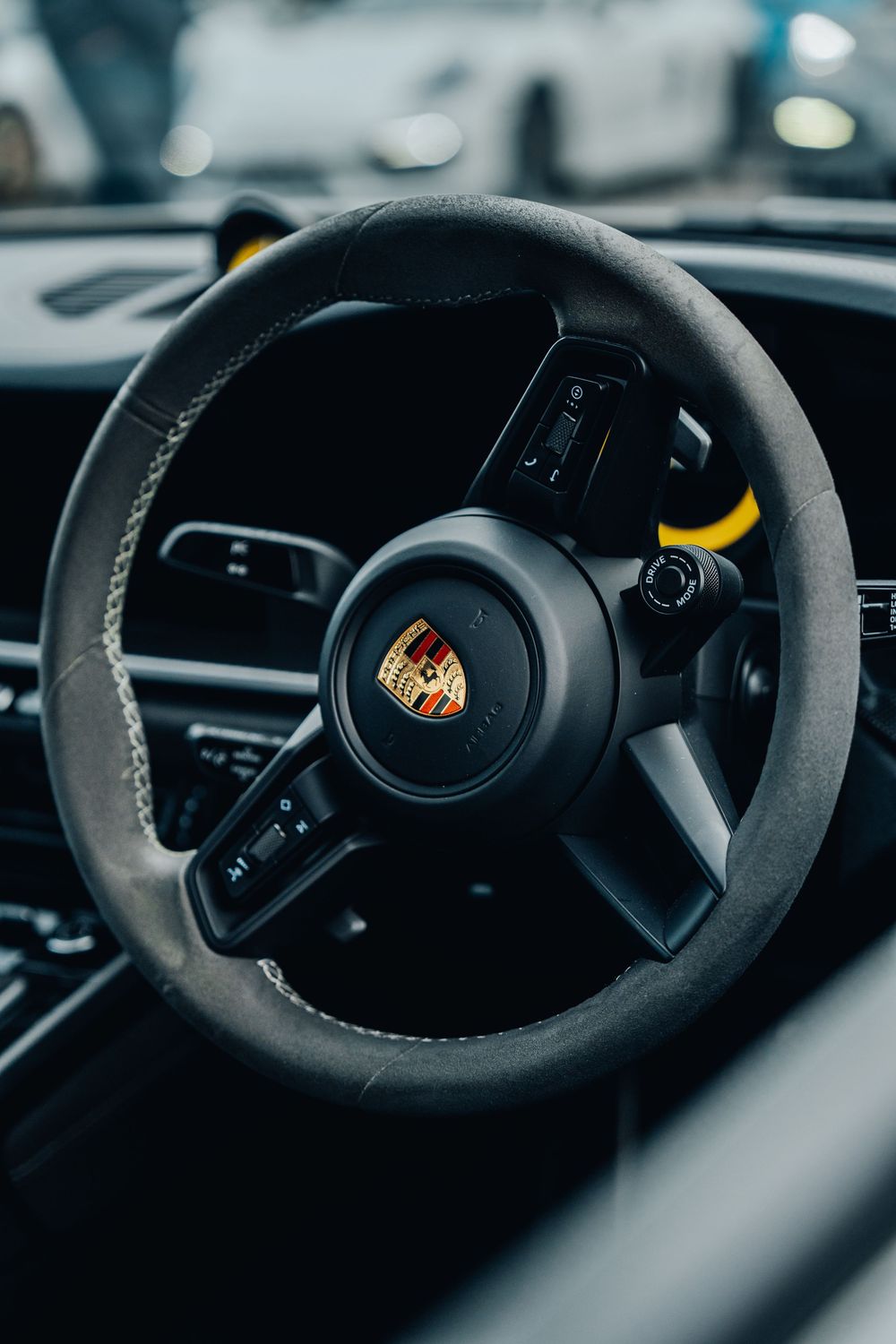 Close-up view of a black Porsche steering wheel with Alcantara material and yellow center marker.