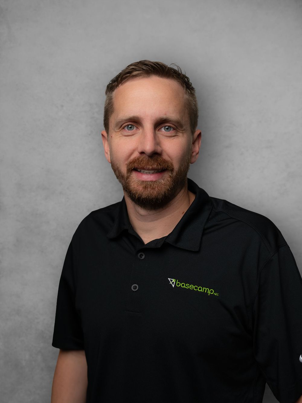 Professional headshot of person in black polo shirt with green company logo against gray background.