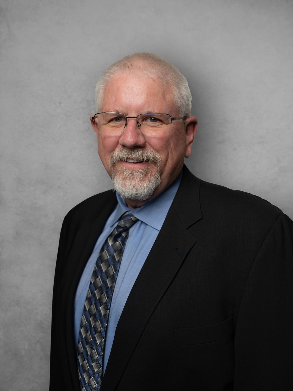 Professional headshots of someone in a dark suit and patterned tie against a gray background.