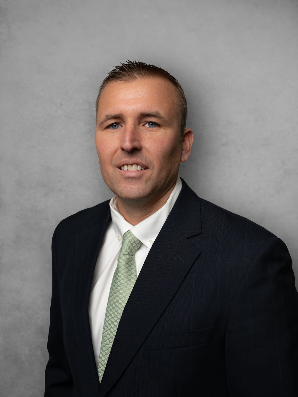 Professional headshot series showing a person in a dark suit and green tie against a gray background.