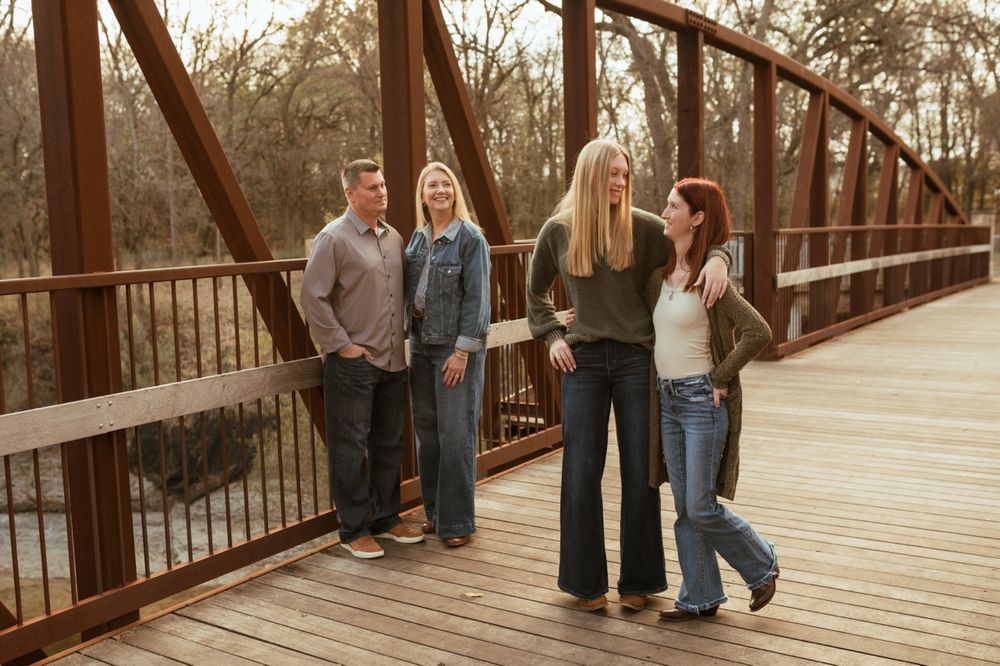 Group of people posing casually on a rustic wooden bridge during golden hour.