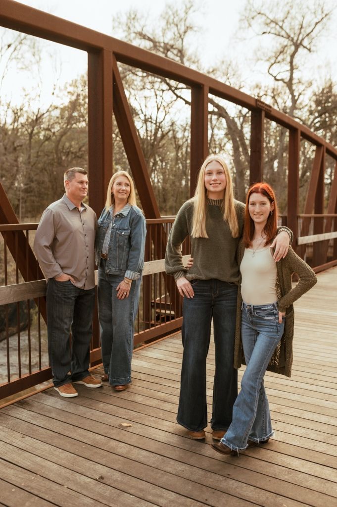 Family members standing together on a wooden deck bridge in casual attire.