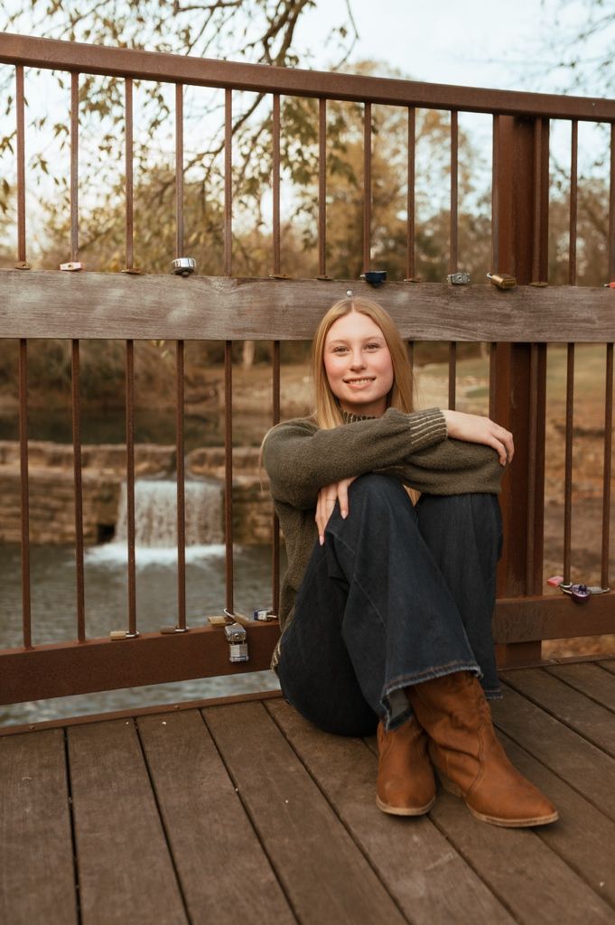 Person sitting on wooden deck wearing boots and casual clothing at sunset.