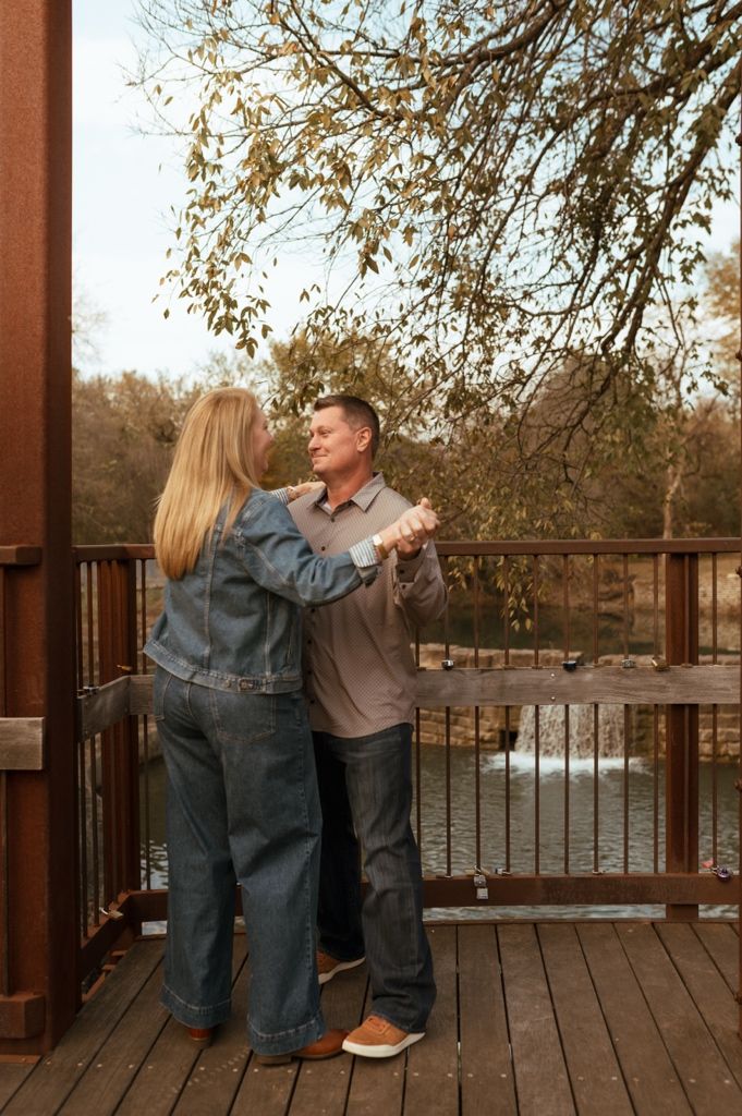 Couple embracing on wooden deck overlooking water during sunset.