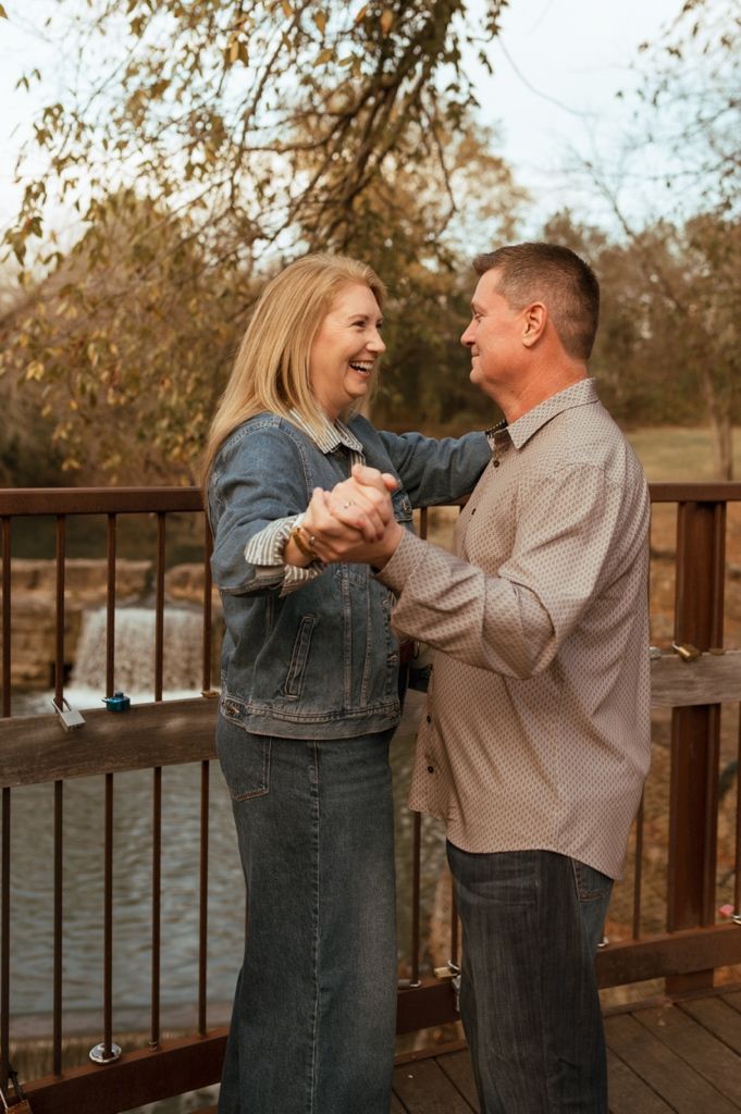 A couple shares a joyful dance moment on a wooden bridge.