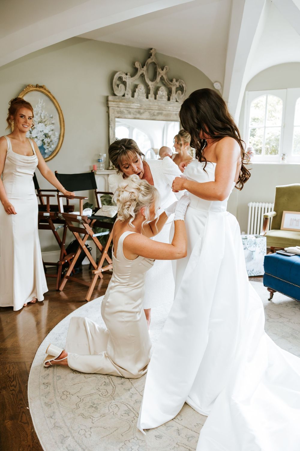 Bridesmaids helping bride into white wedding gown in elegant room with ornate mirror and neutral decor. Markree Castle Sligo