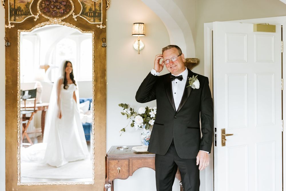 Emotional groom wiping tears as bride in white gown reflects in ornate gold mirror during wedding first look. Markree Castle Sligo