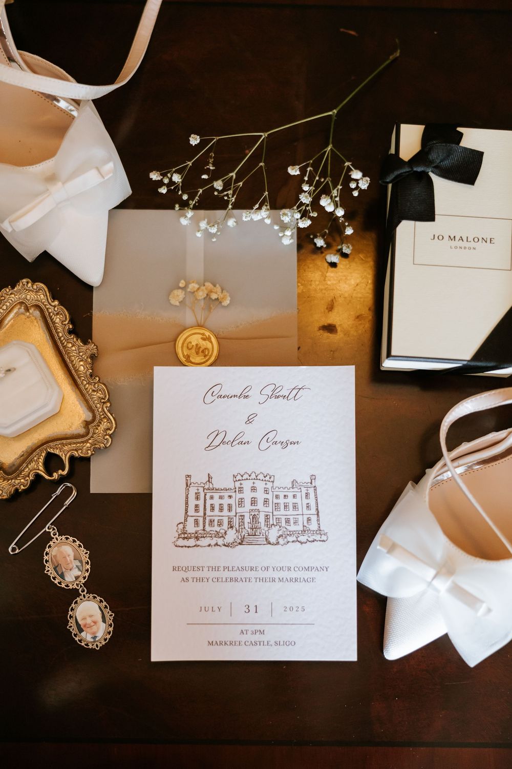 Elegant wedding invitation flatlay with Jo Malone box, white heels, gold frame, and baby's breath on dark wood. Markree Castle Sligo