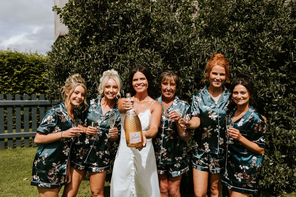 Bride in white dress with bridesmaids in floral robes celebrating with champagne outdoors. Markree Castle Sligo