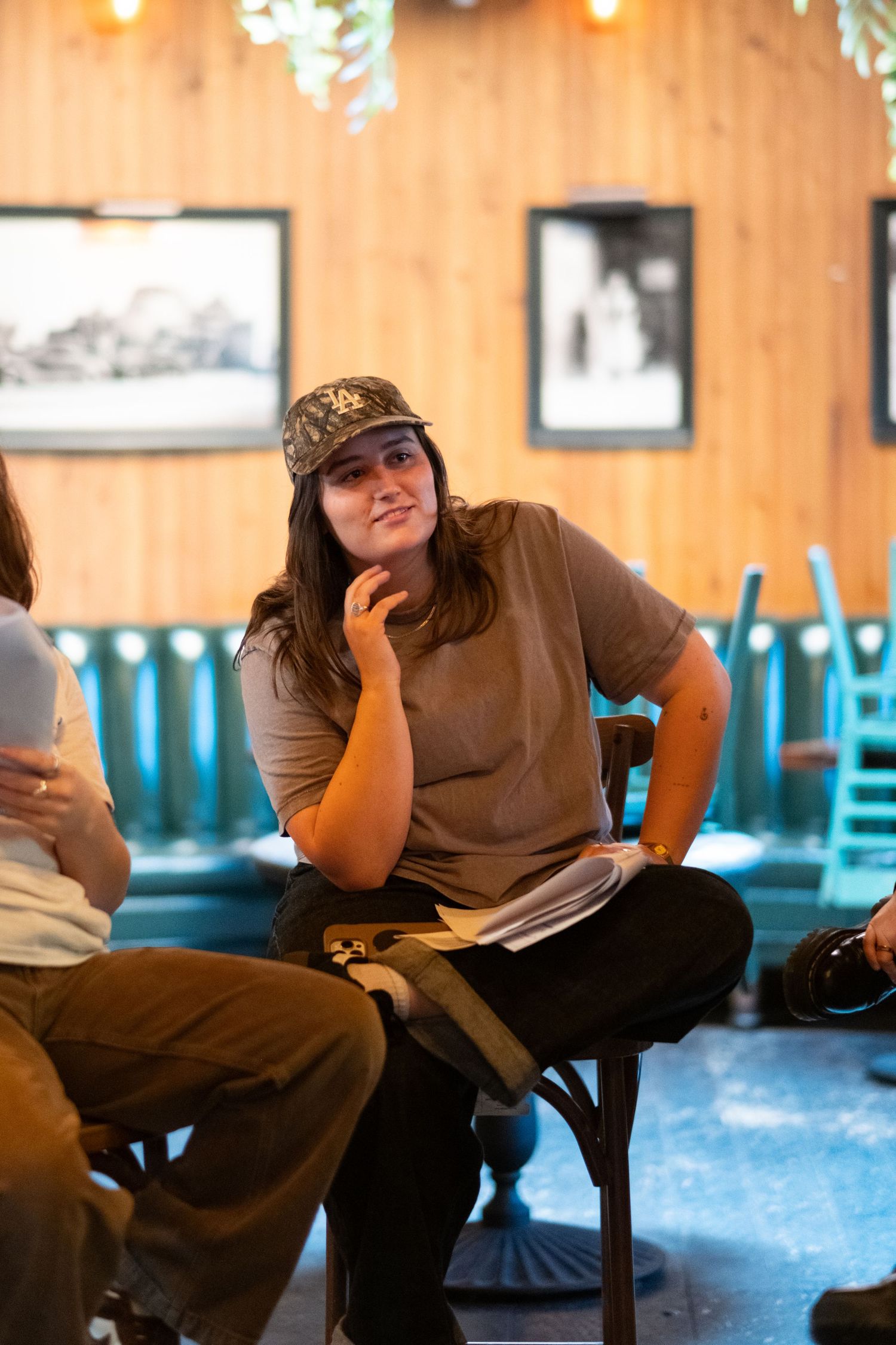 A person in brown attire sits casually on blue chairs in a dimly lit restaurant setting.