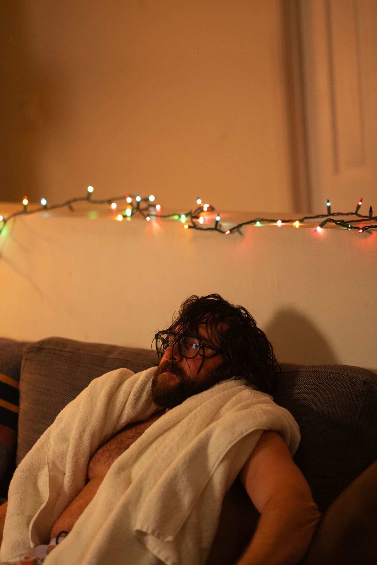 A person sleeps peacefully on a couch under warm string lights creating a cozy atmosphere.
