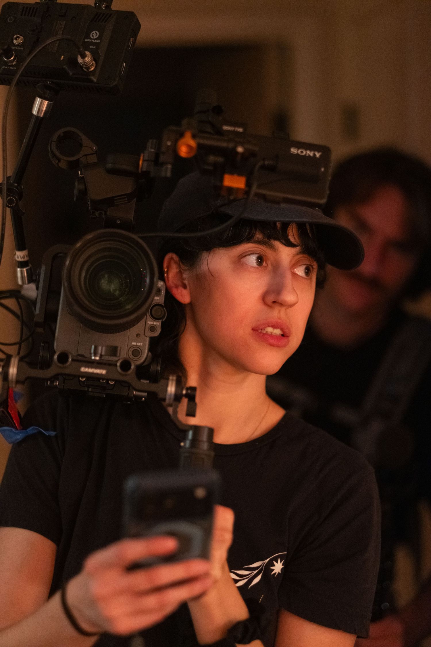 Camera operator wearing black t-shirt and cap films with professional Sony equipment in low light setting.