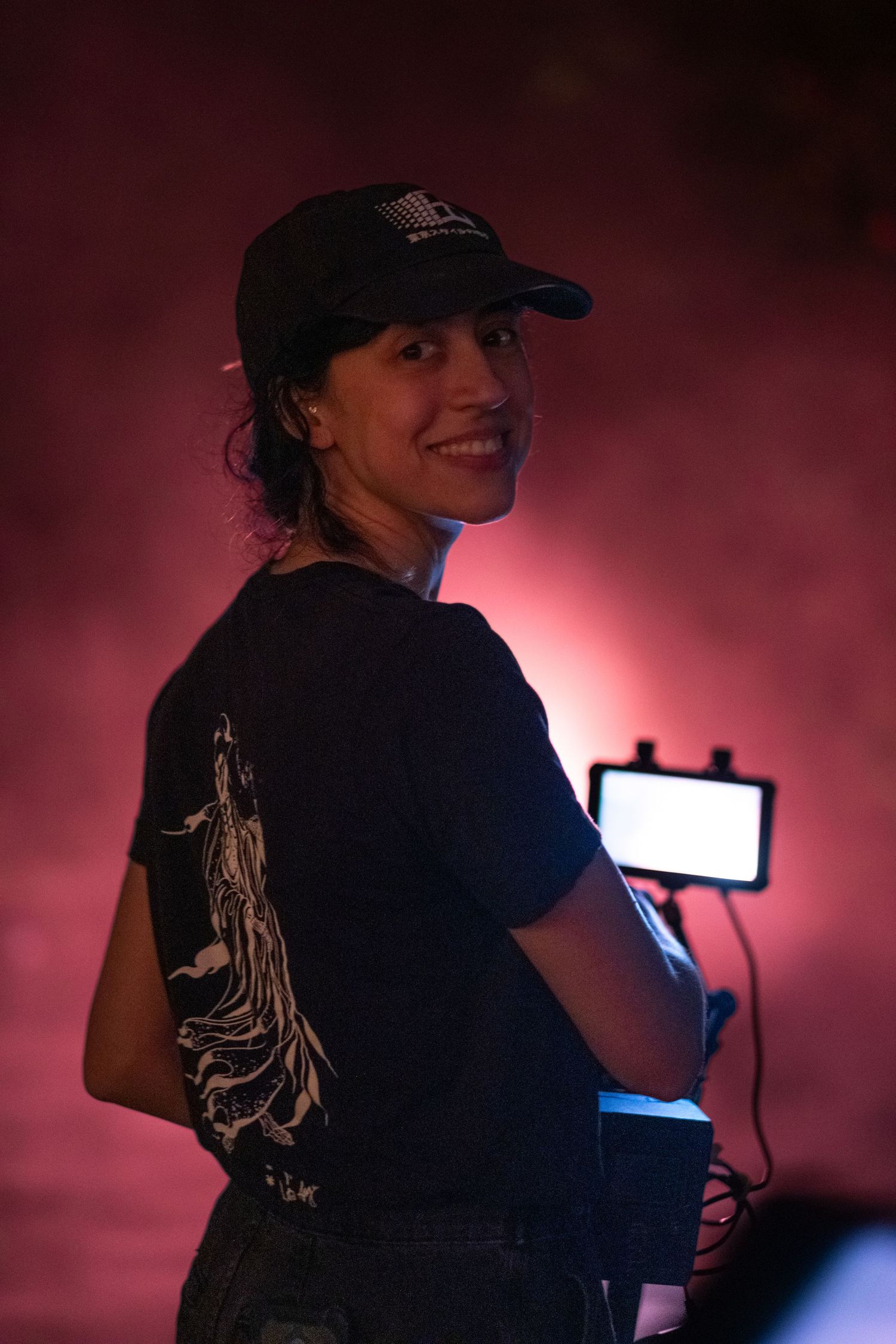 Camera operator in dark clothing silhouetted against pink lighting while filming.