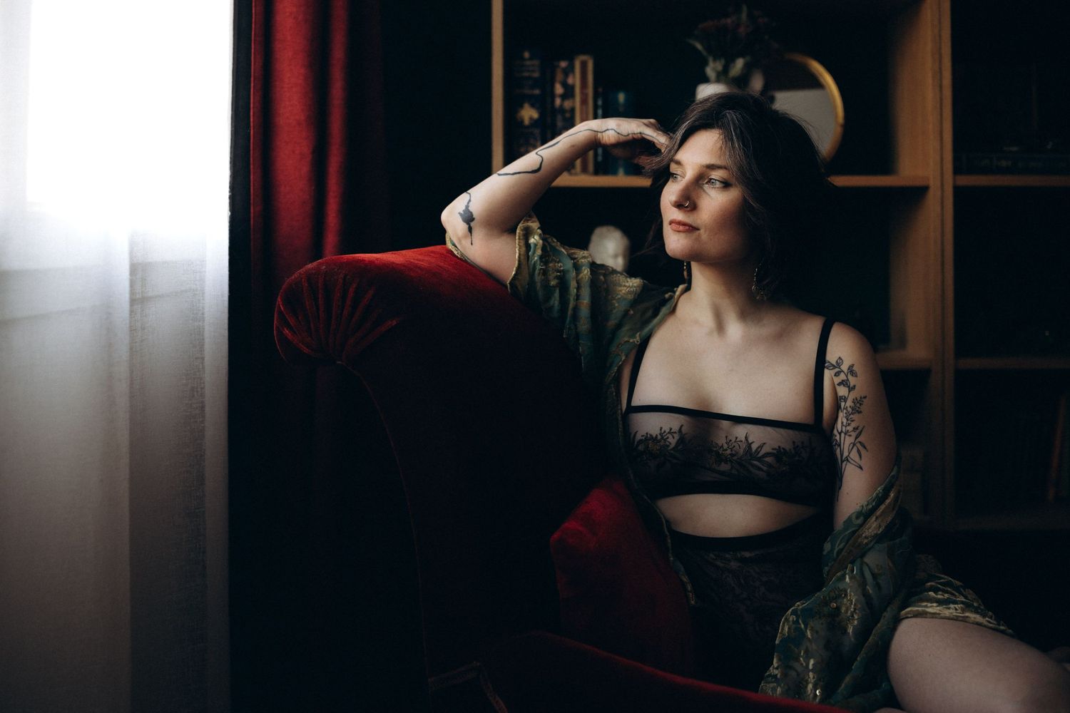 A person in dark lingerie poses dramatically against a wall in moody lighting creating an artistic boudoir portrait.
