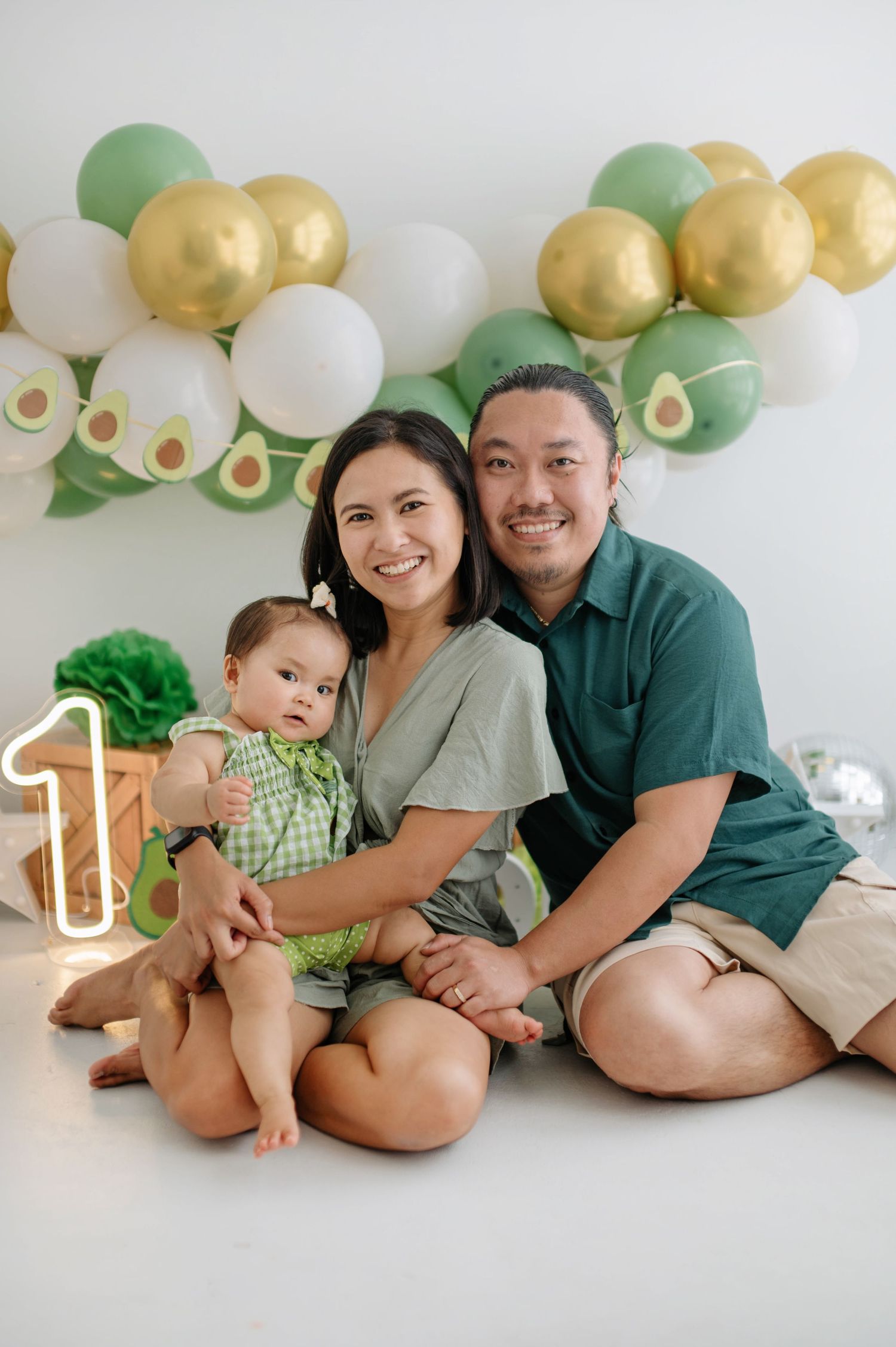 Family photo session with avocado-themed decorations featuring green and gold balloons against white backdrop.