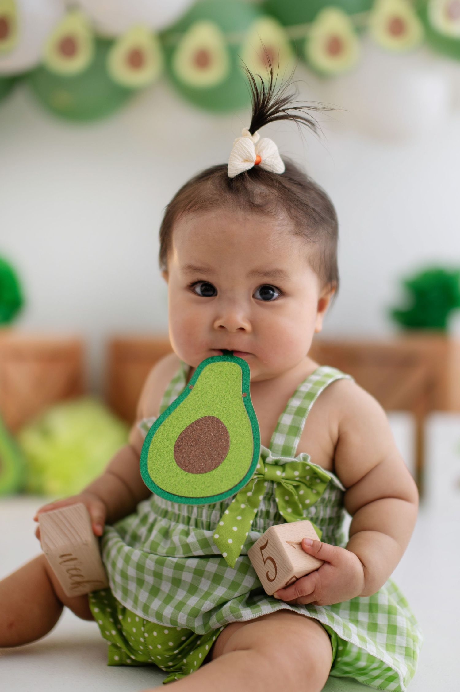 Baby wearing green gingham outfit with avocado design during themed photoshoot.