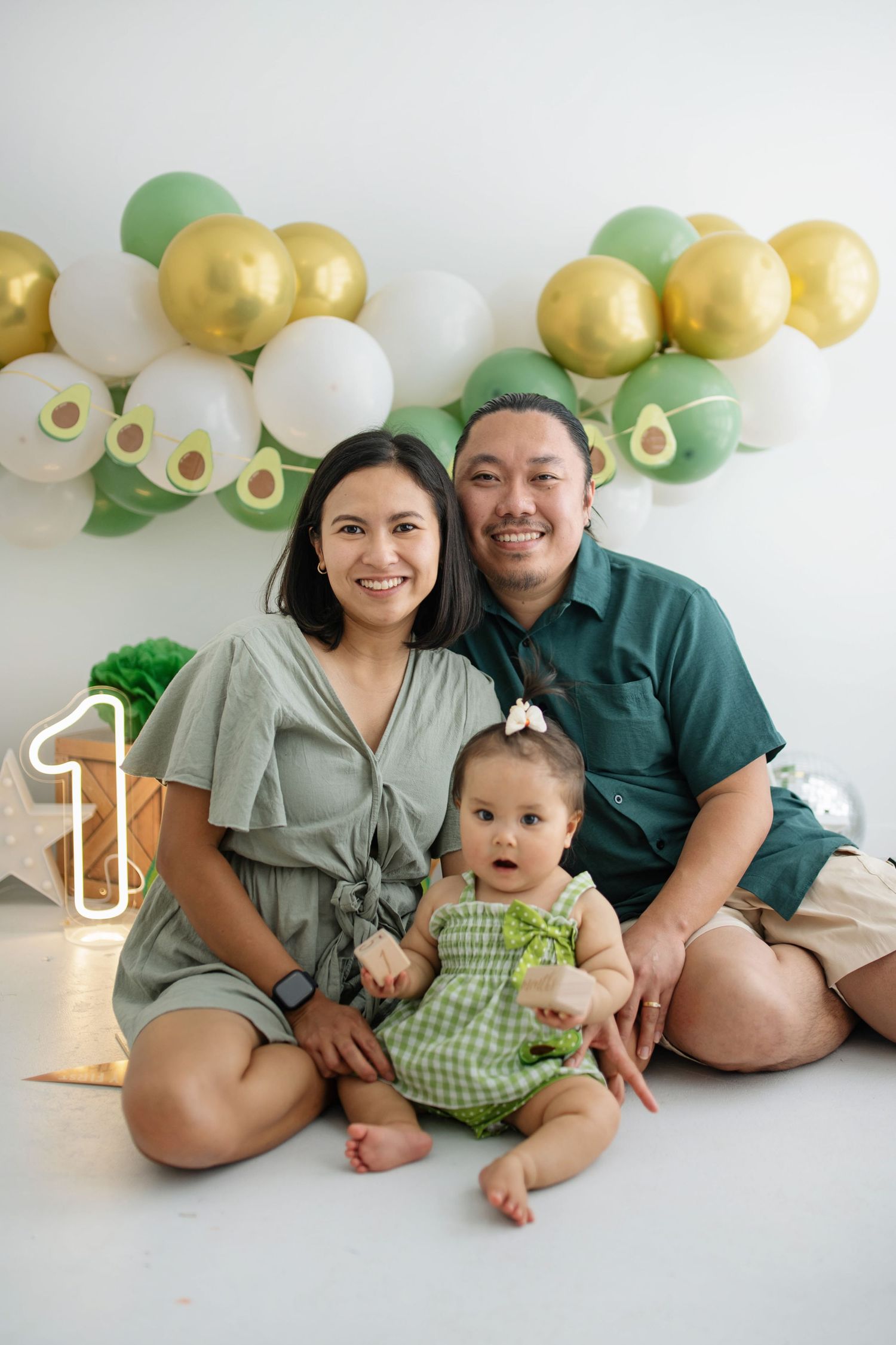 Family posing together on floor with avocado-themed balloon decorations for milestone photoshoot.