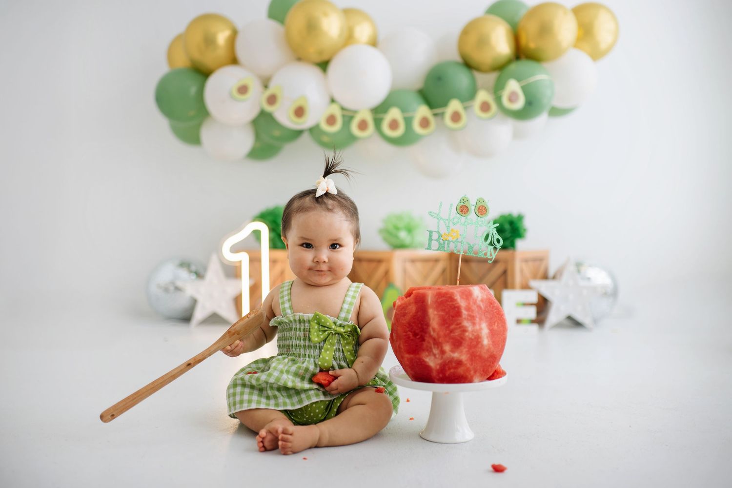 A baby in green sits on a white backdrop with St. Patrick's Day themed decorations and balloons.