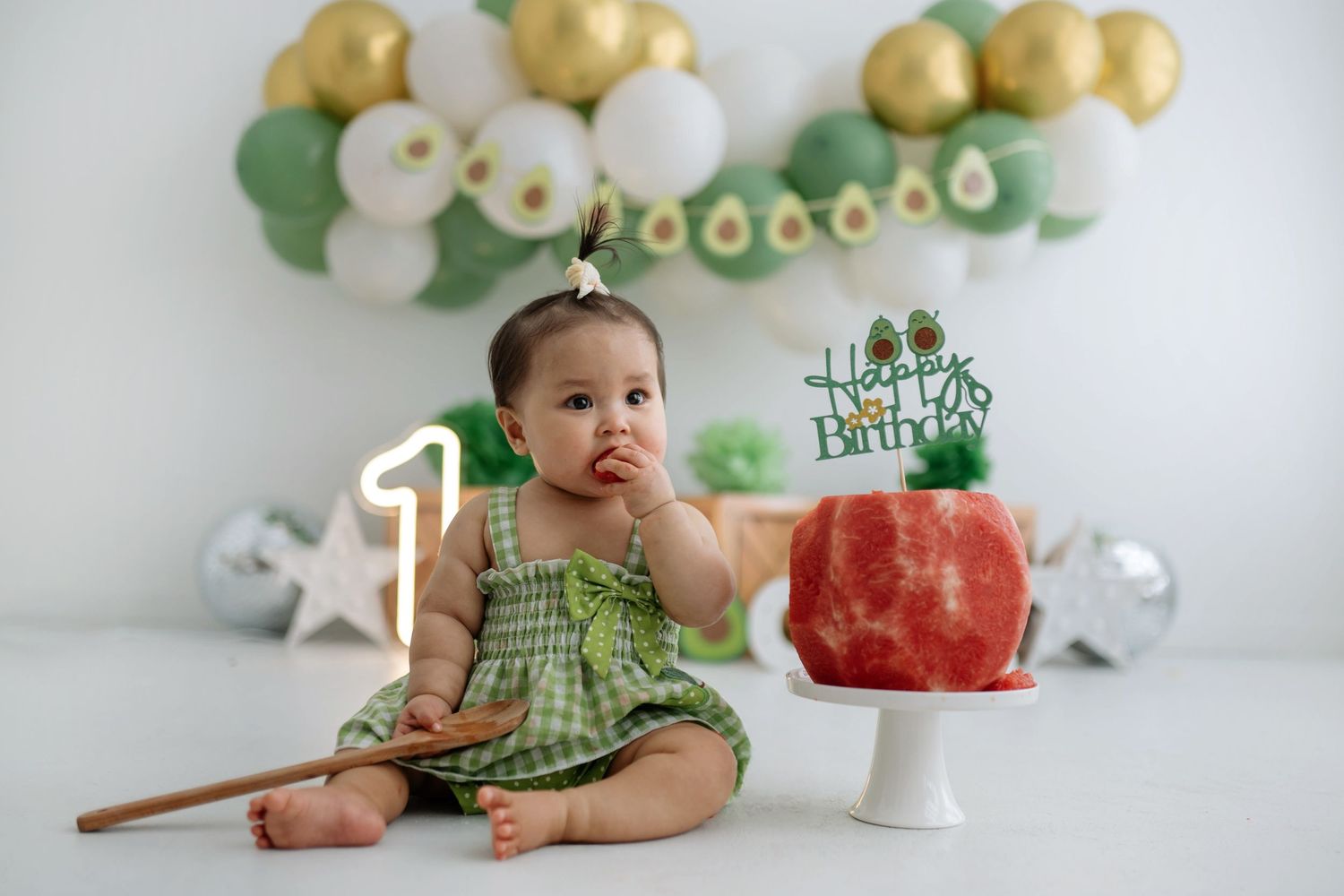 A series of baby milestone photos showing growth and development in a green dress against a white backdrop with balloons.