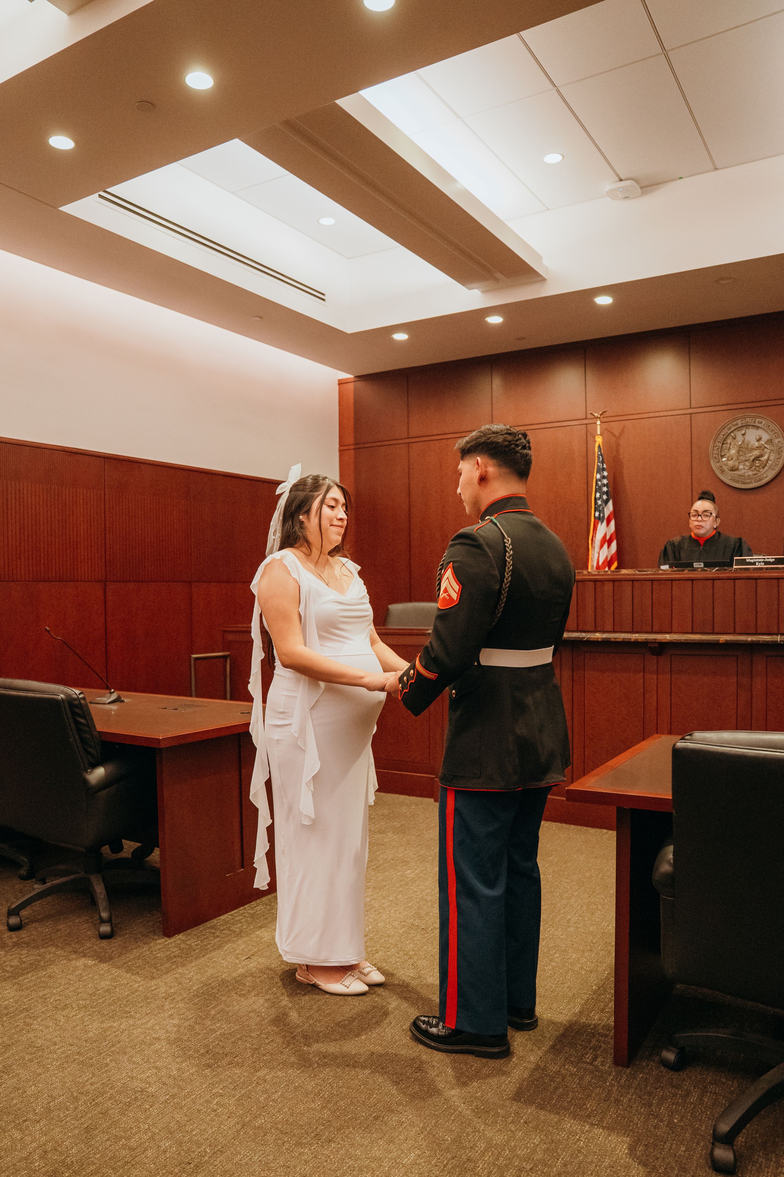 A couple in formal attire participates in a civil ceremony in a courthouse setting.