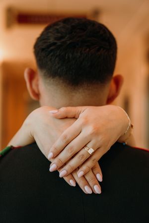 Close-up view of hands wearing wedding rings embracing against a warm brown background.