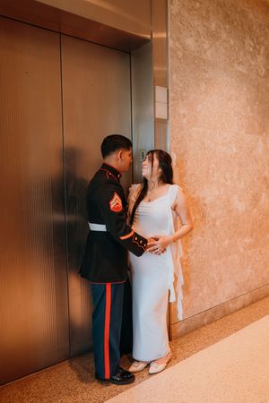 A couple in formal attire share an intimate moment against a textured wall in a hallway.
