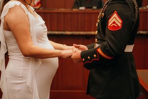 A group in formal dress attends a military wedding ceremony with a Marine in dress uniform standing at attention.