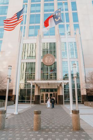 Modern glass building entrance with American flags flying on tall poles against a bright facade.